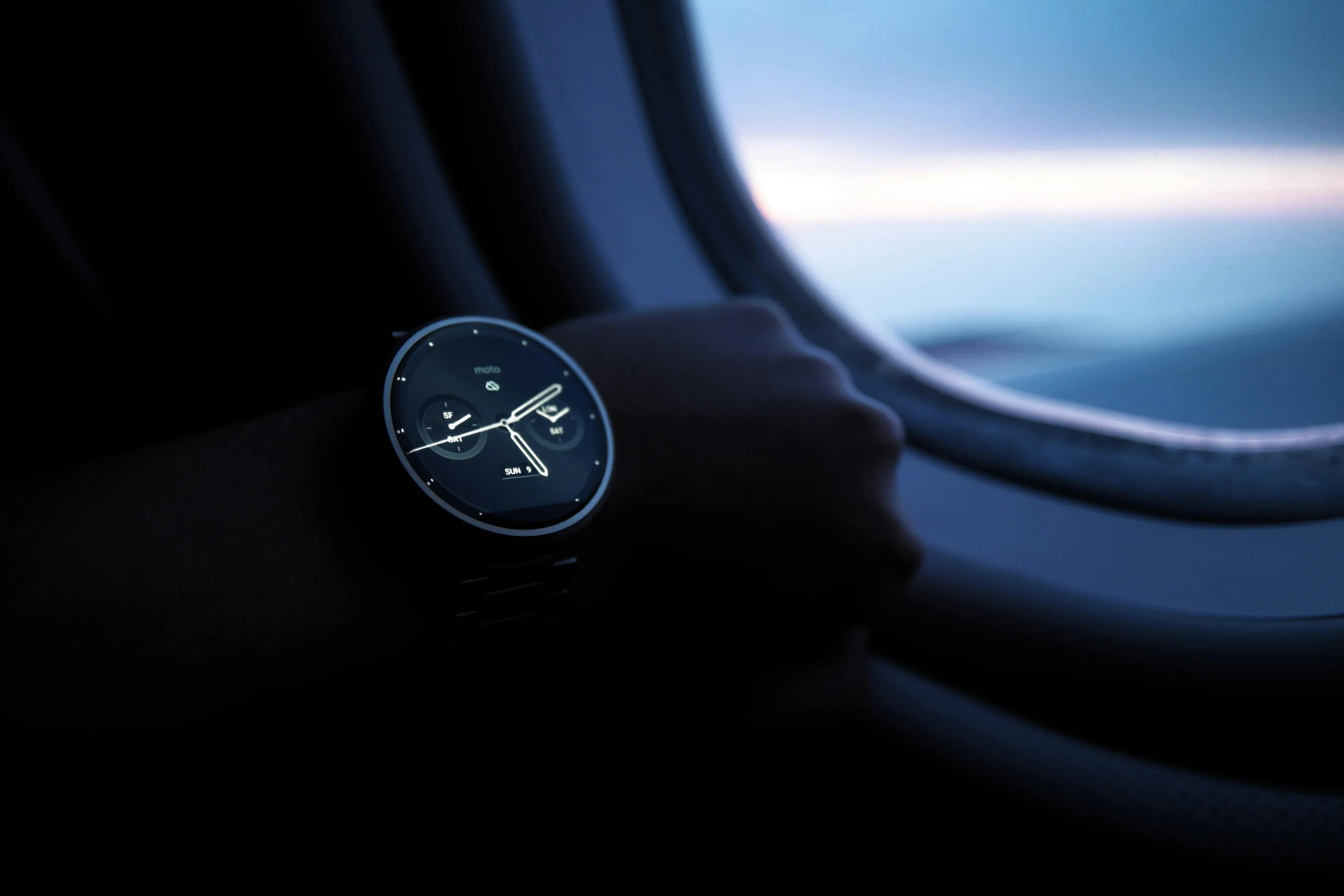 Montre connectée affichant l'heure sur le poignet d'un utilisateur, avec une vue sur le hublot d'un avion en arrière-plan.
